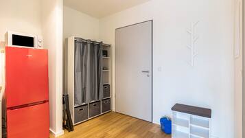 Una habitación compacta con un refrigerador rojo, un armario gris, una puerta blanca y una pequeña estantería blanca.