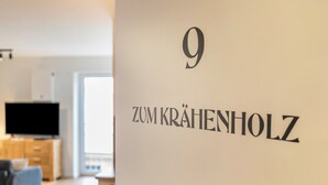 Una habitación con un ventanal grande, un televisor de pantalla plana y una pared con el número 9 y el texto 'Zum Krähenholz'.