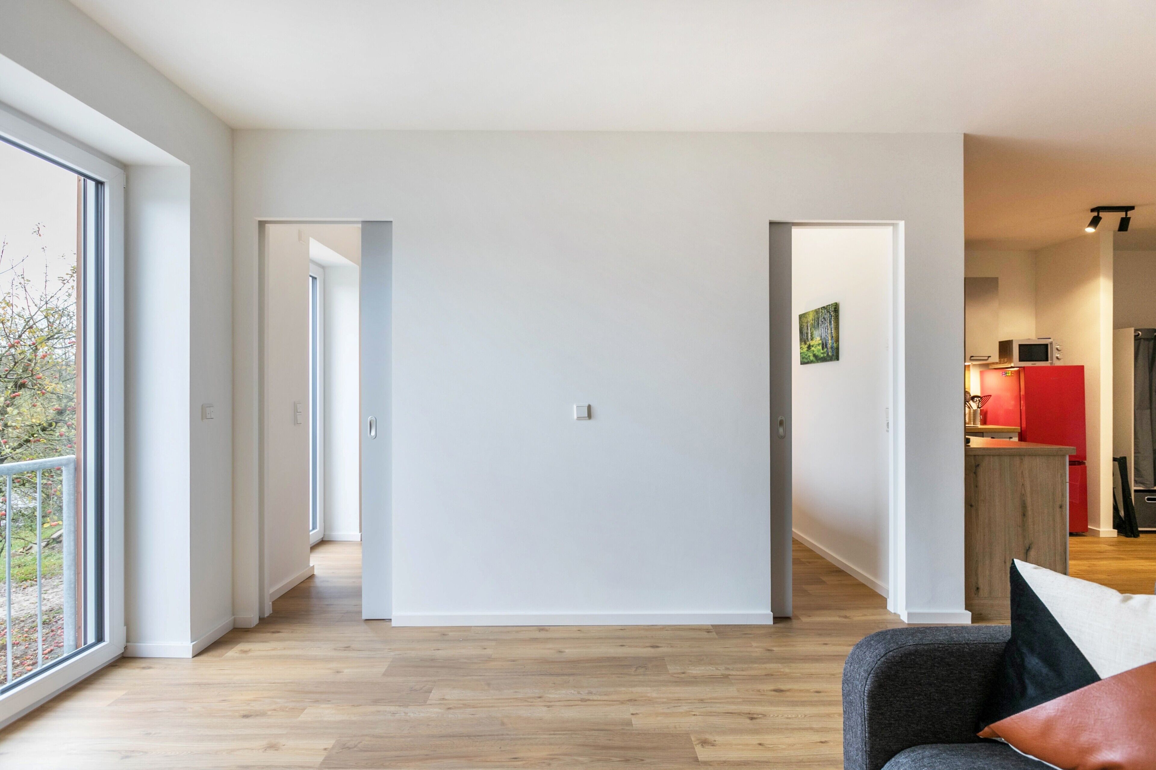 Un interior moderno con piso de madera, un sofá gris y una zona de cocina roja.