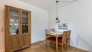 Un comedor con mesa y sillas de madera, un armario con puertas de cristal y una lámpara colgante.