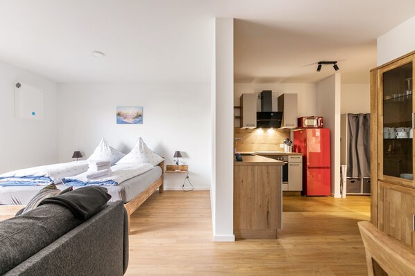 Een knus verblijf met een bed, een klein zitaapje, een kitchenette met een rode koelkast en een houten kast.