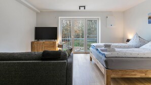 Un dormitorio con una cama, televisor, sofá y una puerta corrediza de vidrio que da a un balcón.