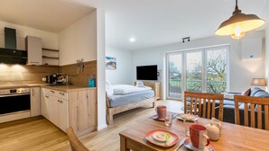 Una cocina moderna con armarios de madera, una mesa de comedor con una taza roja y una cama con un televisor al fondo.