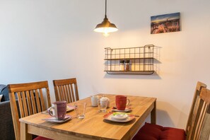 A dining table with chairs, a hanging light, a wall-mounted shelf, and a painting.