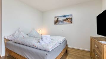 A bedroom with a bed, a wooden dresser, a painting on the wall, and a television.