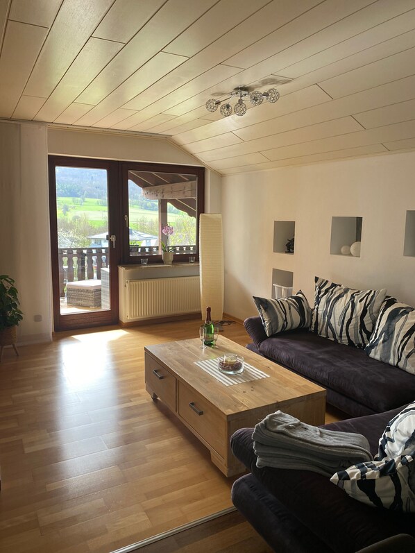 Un salon avec une table basse en bois, un canapé, une vue à travers une porte vitrée et un ventilateur de plafond.