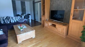 Ein Wohnzimmer mit Couch, Fernseher auf Holzständer, Couchtisch aus Holz und einer Vitrine.