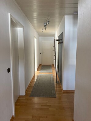 Käytävä, jossa on puulattia, harmaa matto, valkoiset seinät ja kattotuuletin.