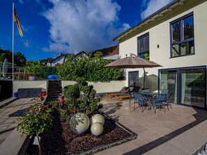 A modern house with a patio, outdoor seating, and a flag. - Apartment 'Zur Quelle' with Private Terrace, Private Garden and Wi-Fi (Plettenberg)