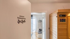 Un pasillo con una puerta de madera, una pared con un letrero y un vistazo a una habitación con un escritorio y una silla.