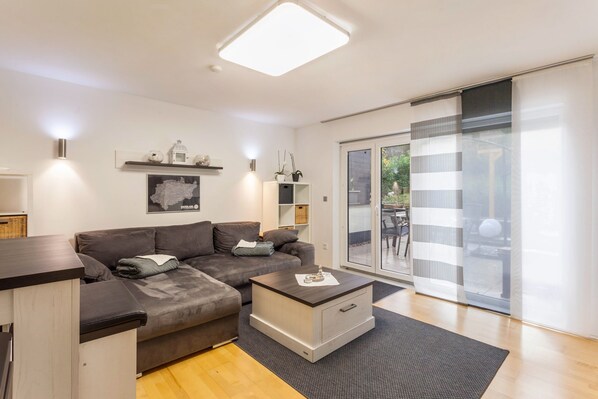 A modern living room with a sofa, coffee table, and a sliding glass door leading to an outdoor area. - Apartment 'Zur Quelle' with Private Terrace, Private Garden and Wi-Fi (Plettenberg)