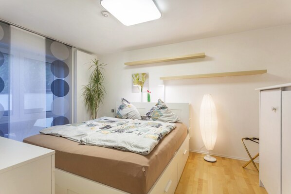Un dormitorio moderno con cama, mesita de noche, lámpara y una planta.