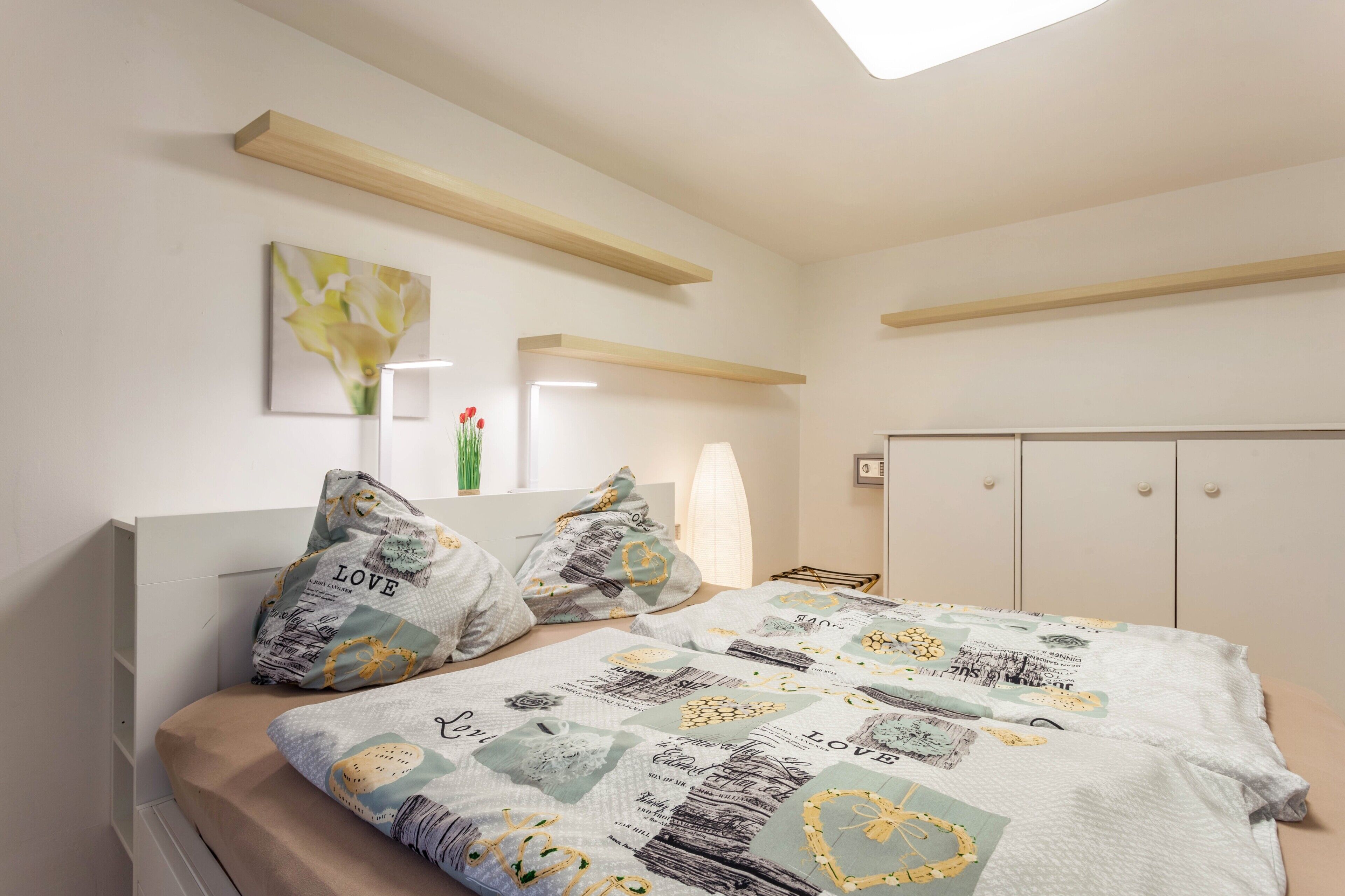 A bedroom with a bed, pillows, a bedside table, a nightstand, a window, and a wardrobe.
