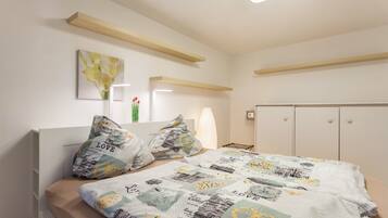 A bedroom with a bed, pillows, a bedside table, a nightstand, a window, and a wardrobe.