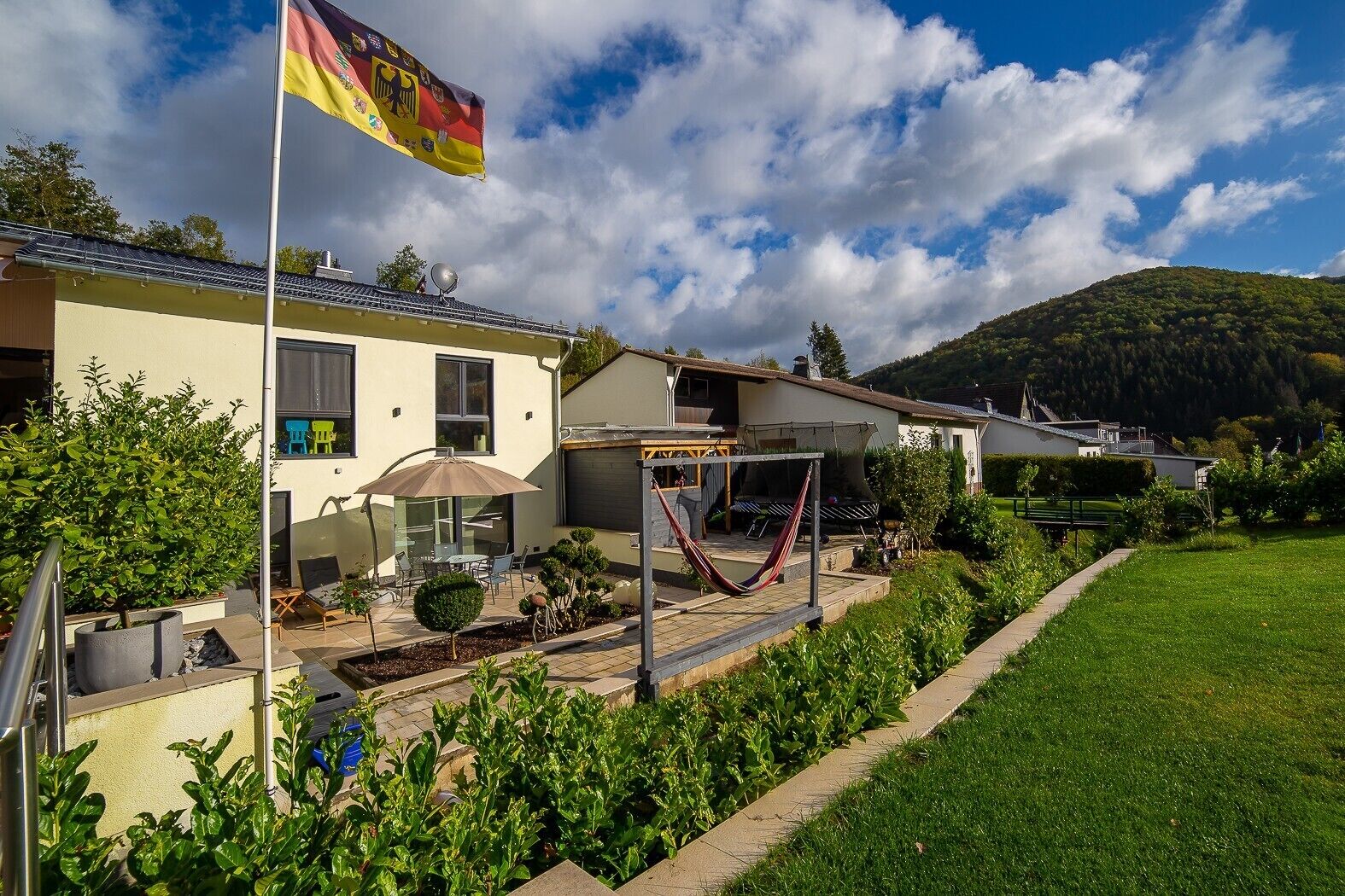 En bostadsfastighet med en flagga, en uteplats med utemöbler och utsikt över en kulle.