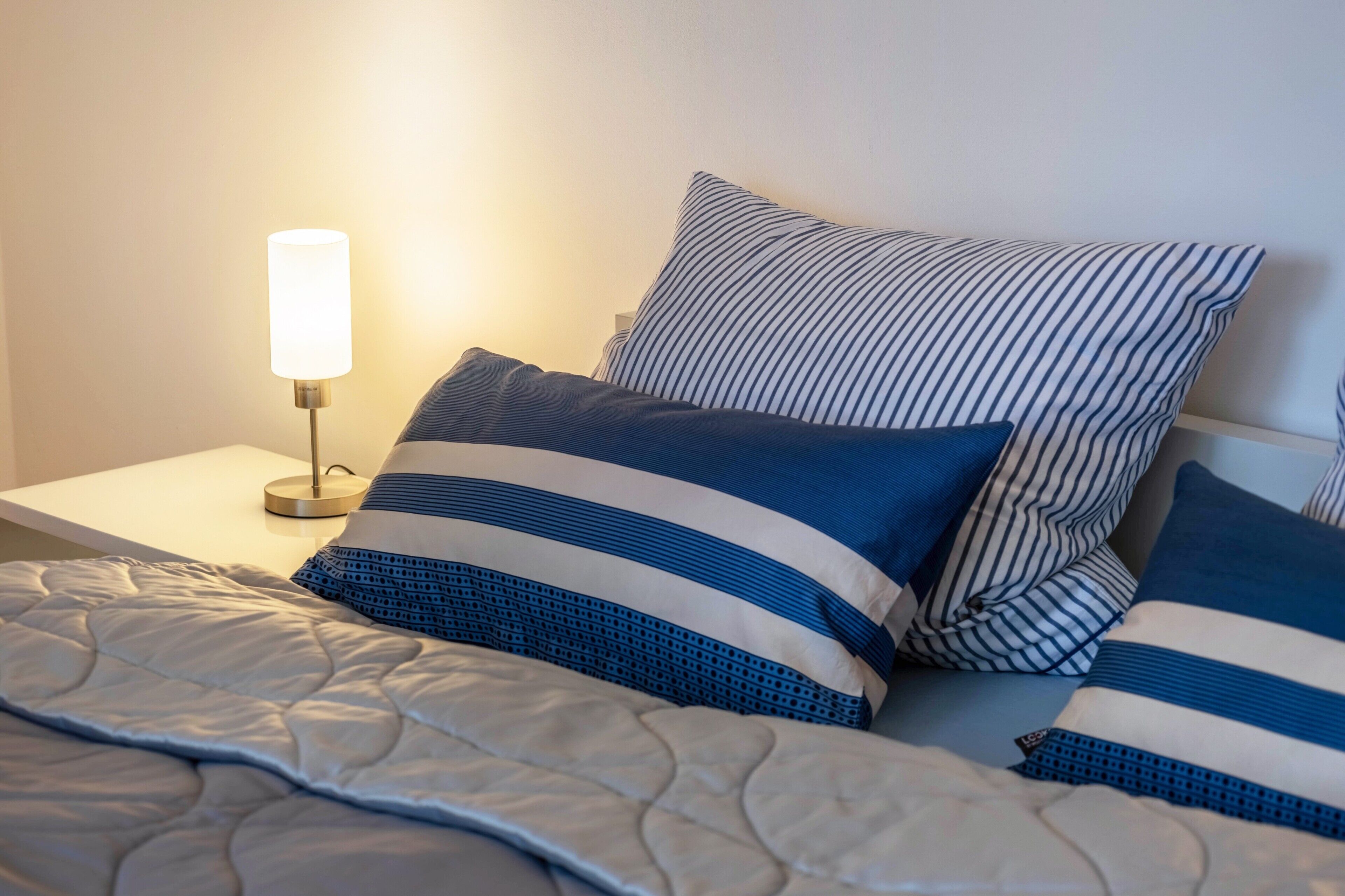 Una cama bien hecha con almohadas a rayas y una lámpara de noche.