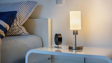 Une table de chevet moderne avec une lampe, une horloge et un oreiller sur un lit.