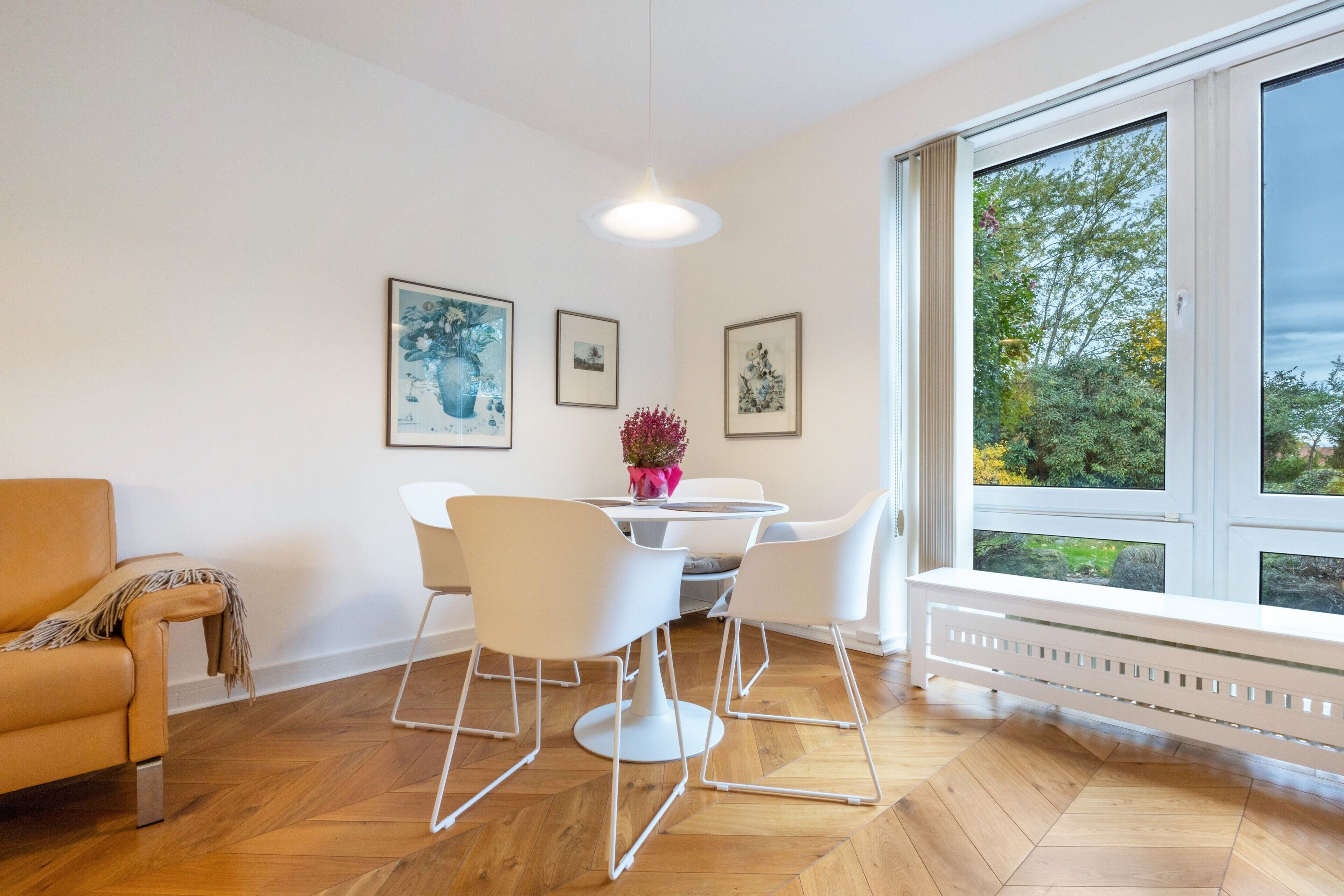 A modern living room with a sofa, a dining table with chairs, and a large window with a view of trees.