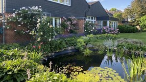 Ein Haus mit Backsteinfassade, einem kleinen Teich und verschiedenen blühenden Pflanzen.