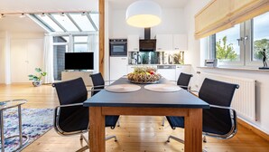 Eine moderne Küche mit einer großen Kochinsel, ein Essbereich mit Tisch und Stühlen und ein Fernseher im Wohnzimmer.