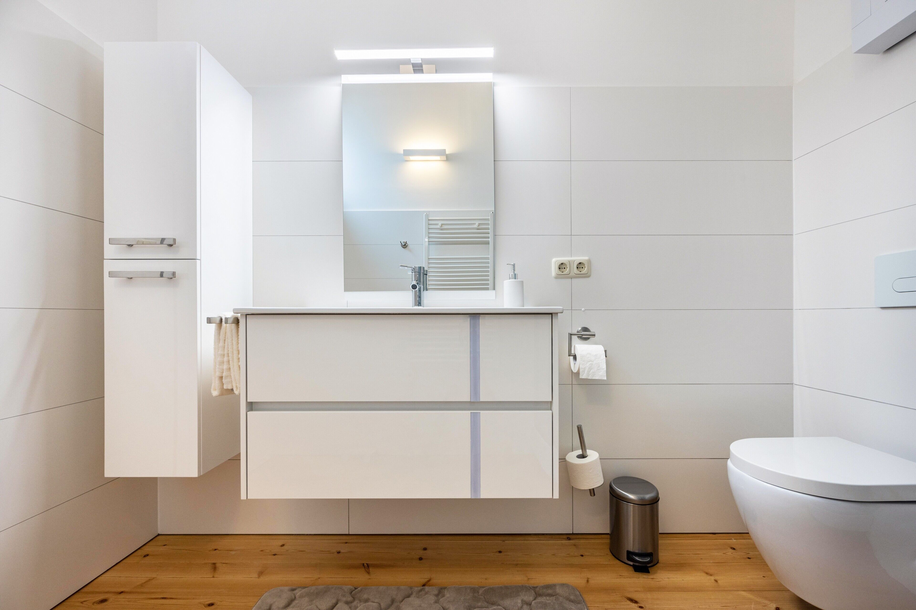 Een moderne badkamer met een witte wastafel, een spiegel, een toilet en een prullenbak.