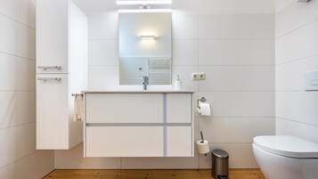 Een moderne badkamer met een witte wastafel, een spiegel, een toilet en een prullenbak.