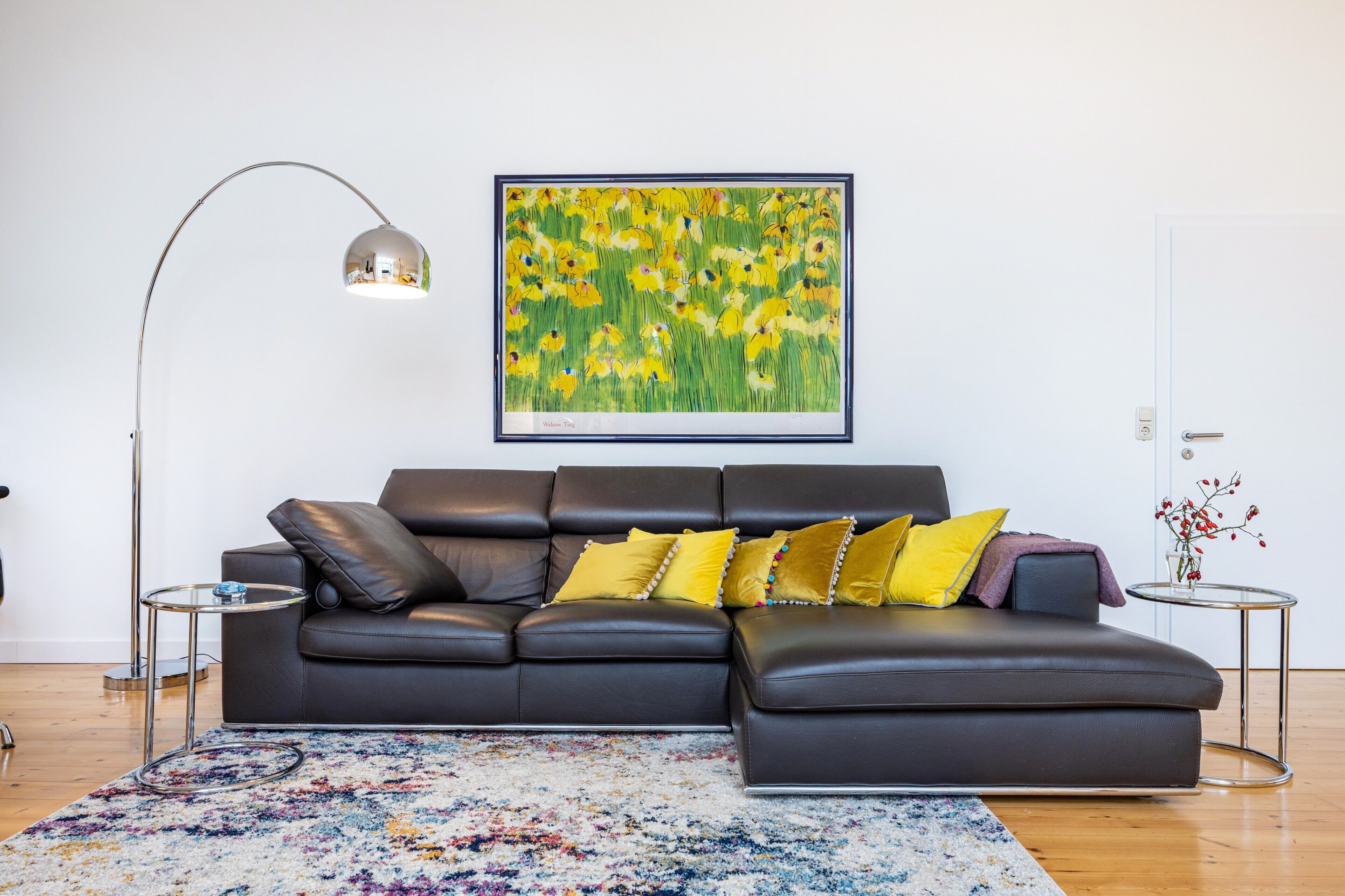 Un salon moderne avec un canapé en cuir noir, un tapis coloré, un tableau encadré et une lampe sur pied.