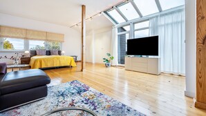 Ein modernes Schlafzimmer mit einem großen Bett, einem Fernseher, einem Oberlicht und Holzboden.