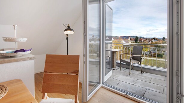 Een balkon met uitzicht op huizen, een stoel, een tafel en een lamp.