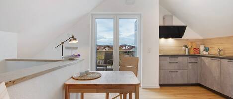 Une cuisine moderne avec une table en bois et une vue sur les maisons, visible à travers une porte vitrée.