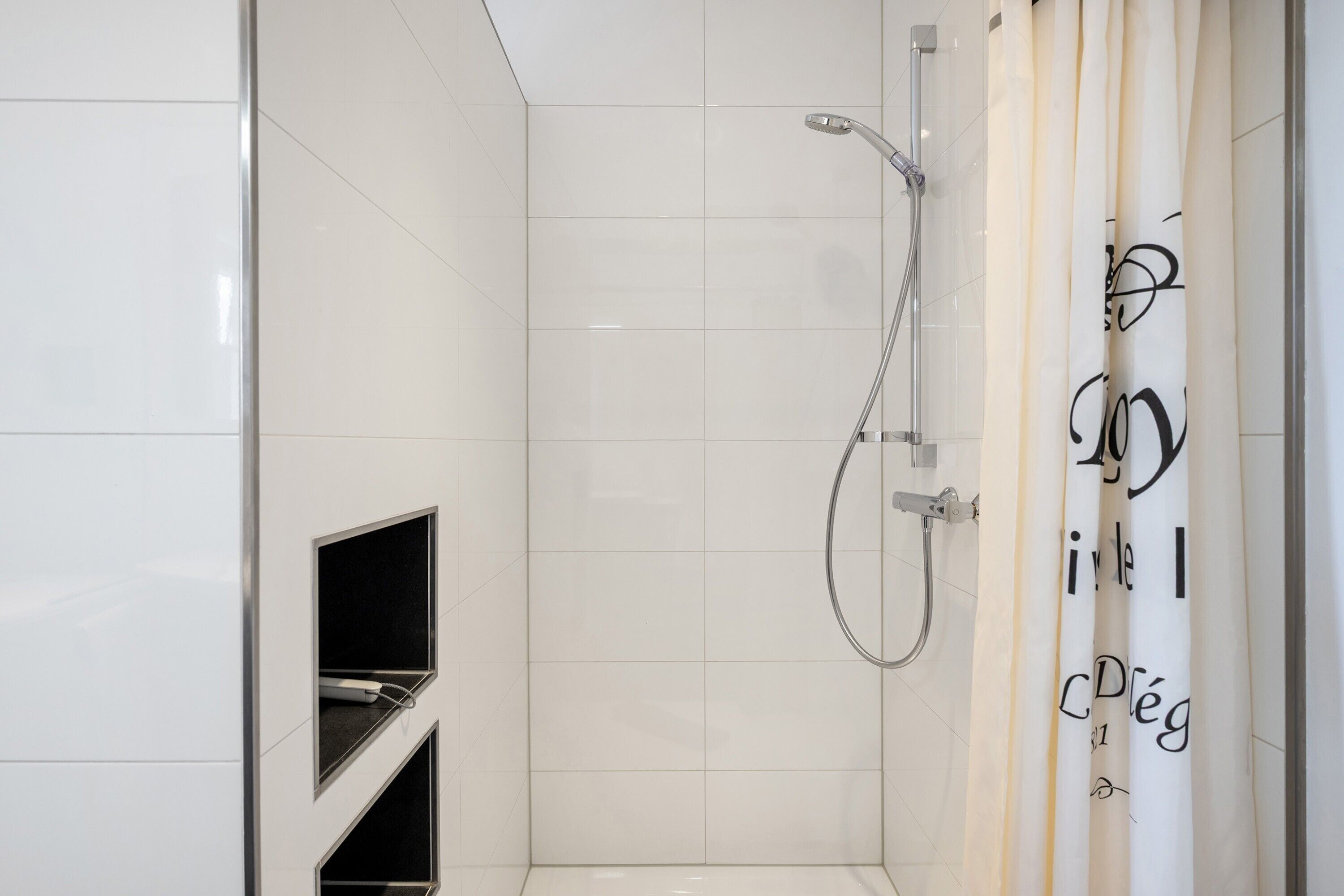 Ein modernes Badezimmer mit weißen Fliesen, einer Dusche inklusive Handbrause und einem Handtuchhalter mit einem Handtuch.