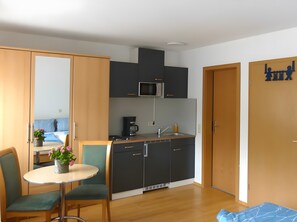 A compact kitchen with a microwave, coffee maker, and sink. There is a dining area with a table and chairs. The room has wooden flooring and a large mirror on one wall. - Studio Apartment 'Ferienwohnung 4a, 30 sqm' with Shared Garden and Wi-Fi (Owingen)
