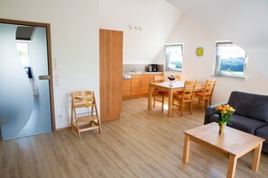 Un salon moderne comprenant un coin repas, un canapé, une table basse agrémentée de fleurs et une cuisine en arrière-plan.
