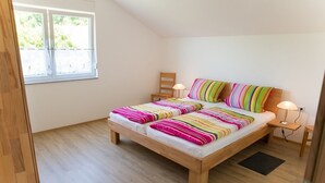 Uma cama de solteiro com estrutura de madeira, duas mesas de cabeceira, uma janela e vista para o verde lá fora.
