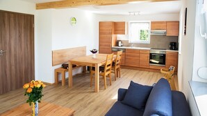 A compact kitchen with wooden cabinets, a dining table with chairs, a sofa, and a small table with a vase of flowers. - Holiday Home 'Haus 1, 80 Qm, 2 Schlafzimmer' with Private Terrace, Shared Garden and Wi-Fi (Owingen)