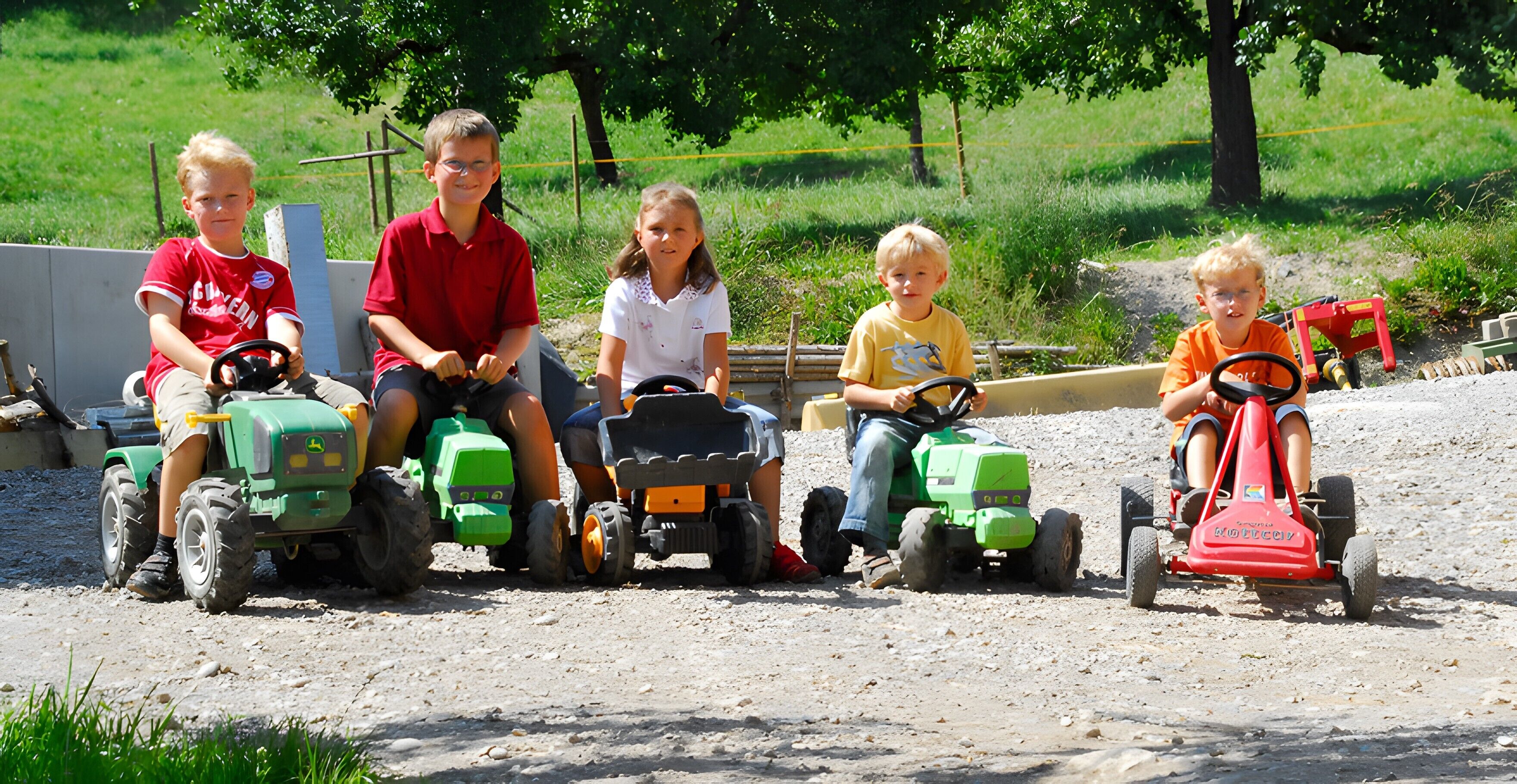Kinder fahren mit Spielzeugtraktoren auf einem Feldweg.