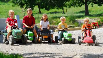 Kinder fahren mit Spielzeugtraktoren auf einem Feldweg.