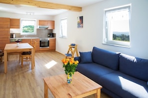 Una cocina moderna con armarios de madera, una mesa de comedor con sillas, un sofá azul y una mesa de centro de madera con un jarrón de flores.