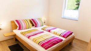 A single bed with a wooden frame, a black rug, and a window with a view of greenery. - Holiday Home 'Haus 1, 80 Qm, 2 Schlafzimmer' with Private Terrace, Shared Garden and Wi-Fi (Owingen)