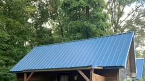 Une cabane rustique dotée d’une véranda, de murs en bois et d’un toit en métal bleu.