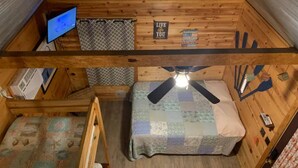 Une cabane confortable avec un lit, un bureau et un ventilateur de plafond.