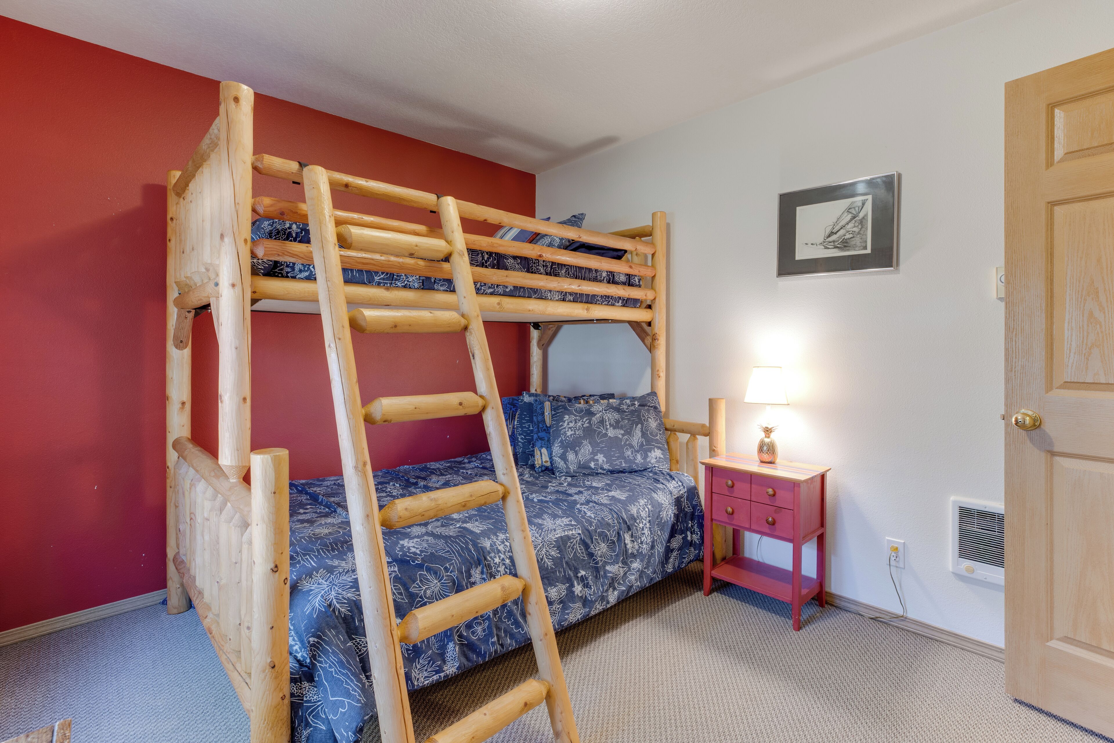Un lit superposé avec une échelle en bois, une table de chevet avec une lampe et un tableau encadré au mur.