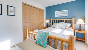 A bedroom with a wooden bed, two bedside tables with lamps, a large wooden door, and a framed picture on the wall. - Kiwanda Cabana - near beach, cute house! Dog OK. (Pacific City)