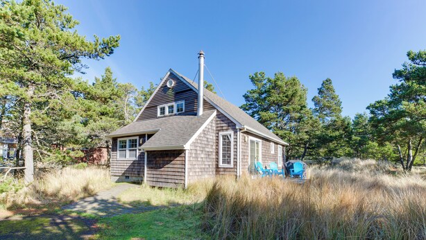 A wooden cabin with a chimney, surrounded by tall grass and trees. - Kiwanda Cabana - near beach, cute house! Dog OK. (Pacific City)