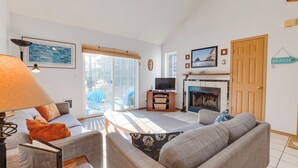 A living room with a sofa, a television, a fireplace, and a sign indicating a beach direction. - Kiwanda Cabana - near beach, cute house! Dog OK. (Pacific City)