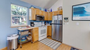 A kitchen with wooden cabinets, stainless steel appliances, a window, and a view of the ocean. - Kiwanda Cabana - near beach, cute house! Dog OK. (Pacific City)