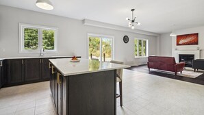 A modern kitchen with dark cabinets, a large island, and a dining area with a red sofa. - Amazing stay near Hamilton-Brantford- Beach Port Dover (Norfolk)