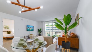 Uma sala de jantar moderna com uma mesa de vidro, cadeiras brancas e uma grande planta em vaso.