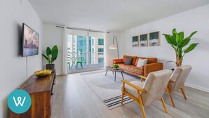 Uma sala de estar moderna com sofá, poltronas, mesa de centro e uma janela grande com vista para a cidade.