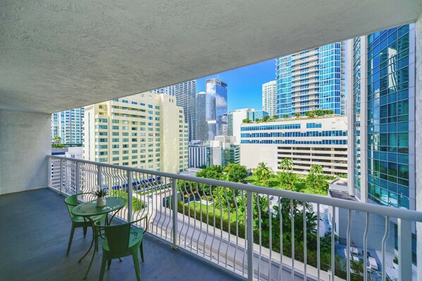 Varanda com vista para edifícios modernos e alto padrão, grade e duas cadeiras verdes.